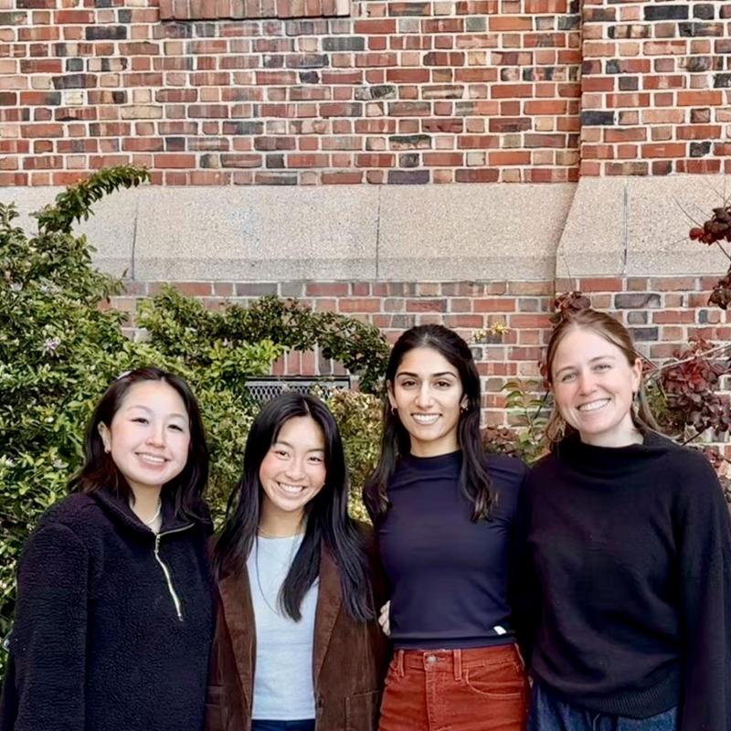 Lilian, Sam, Anisha, and Morgan are seen standing in the middle of the frame, facing the camera and smiling. 